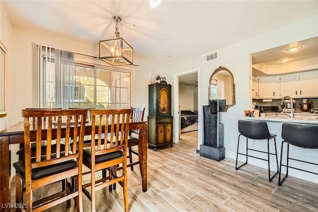 dining room featuring a healthy amount of sunlight, visible vents, light wood finished floors, and a chandelier