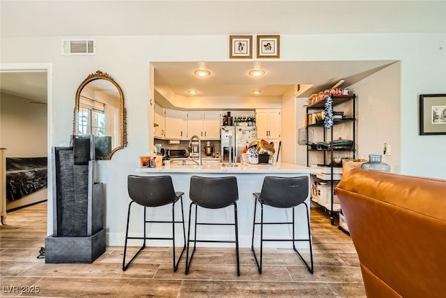 kitchen with visible vents, wood finish floors, stainless steel fridge with ice dispenser, a peninsula, and a kitchen breakfast bar