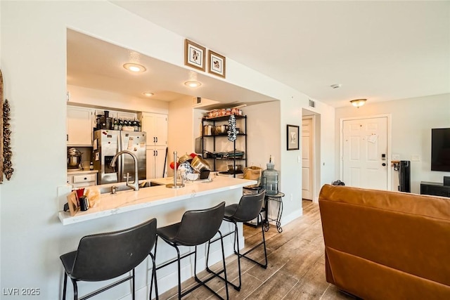 kitchen with a kitchen bar, a peninsula, wood finished floors, stainless steel fridge, and white cabinetry