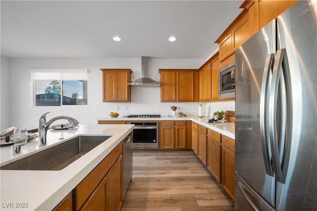 kitchen featuring stainless steel appliances, light hardwood / wood-style floors, sink, and wall chimney range hood