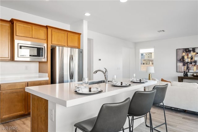 kitchen with a kitchen island with sink, a kitchen bar, light hardwood / wood-style floors, and appliances with stainless steel finishes