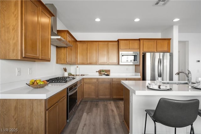 kitchen with dark hardwood / wood-style floors, sink, a kitchen bar, stainless steel appliances, and wall chimney exhaust hood