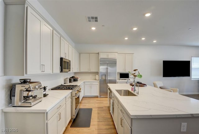 kitchen with sink, high quality appliances, light stone countertops, white cabinets, and a center island with sink