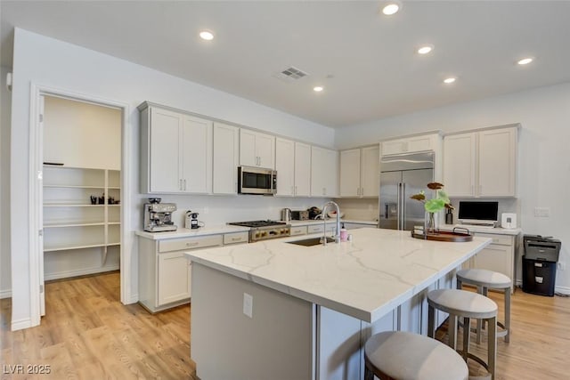 kitchen featuring sink, appliances with stainless steel finishes, light stone countertops, an island with sink, and white cabinets