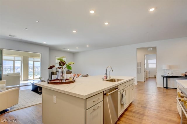 kitchen featuring dishwasher, sink, a kitchen island with sink, and light hardwood / wood-style flooring