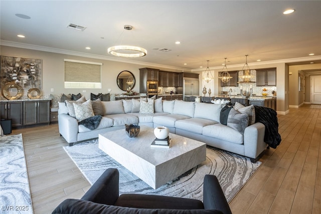 living room with crown molding, a chandelier, and light wood-type flooring