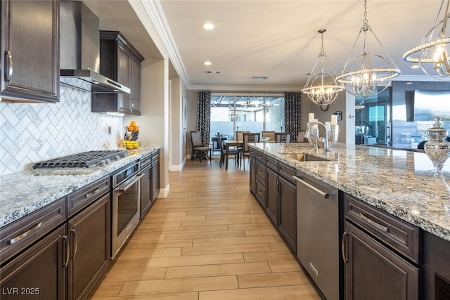 kitchen with pendant lighting, crown molding, wall chimney exhaust hood, and appliances with stainless steel finishes