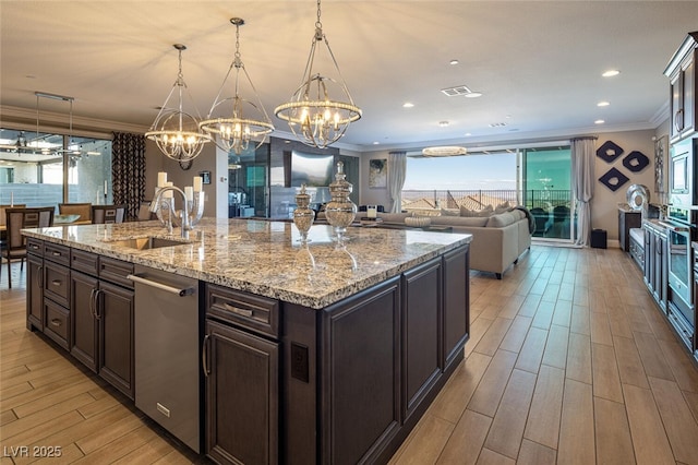 kitchen with ornamental molding, a kitchen island with sink, sink, and hanging light fixtures