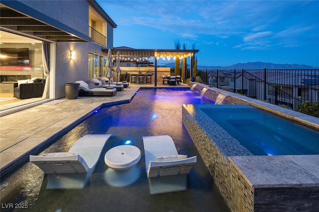 pool at dusk with an outdoor bar, a patio, a mountain view, pool water feature, and an in ground hot tub