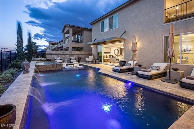 pool at dusk with a patio area, an outdoor living space with a fire pit, pool water feature, and an in ground hot tub