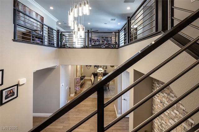 staircase featuring a high ceiling, ornamental molding, hardwood / wood-style floors, and a chandelier