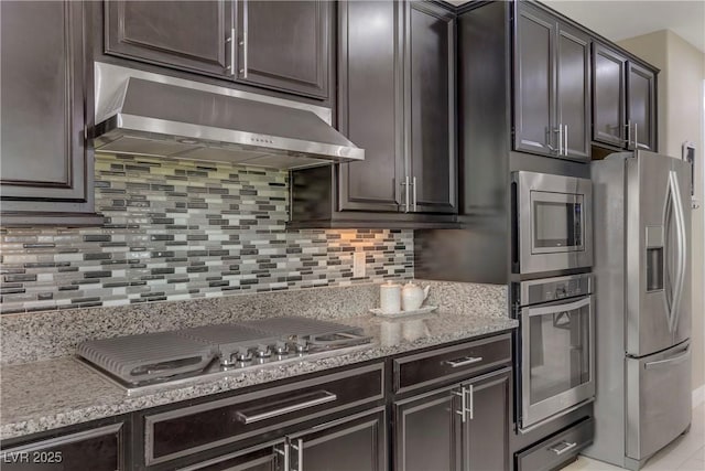 kitchen featuring tasteful backsplash, stainless steel appliances, light stone countertops, and dark brown cabinets