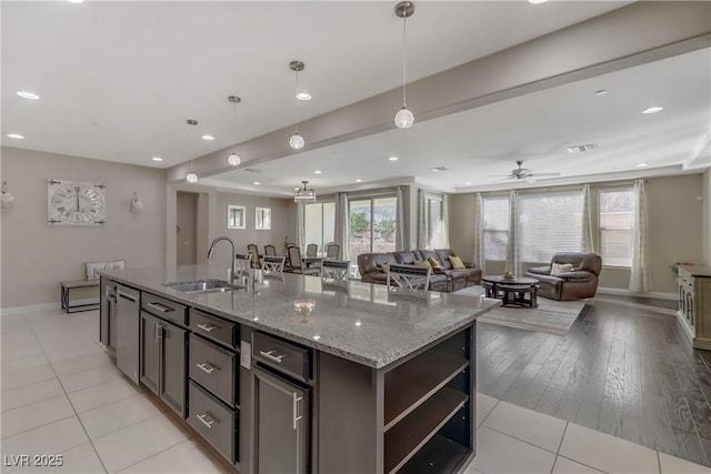 kitchen featuring sink, light stone counters, dark brown cabinets, pendant lighting, and a kitchen island with sink