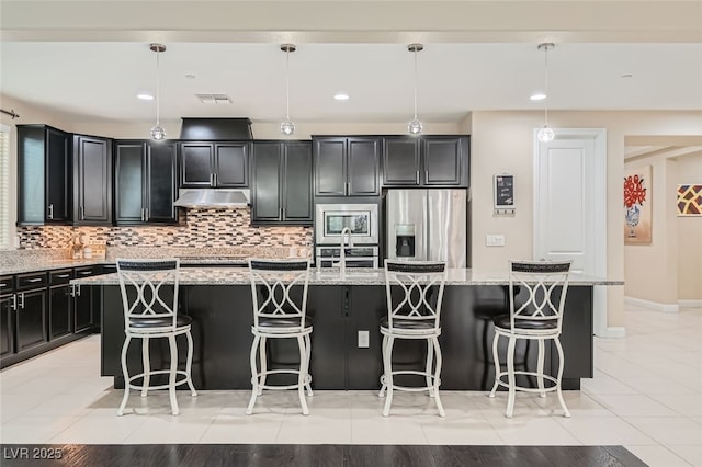 kitchen with appliances with stainless steel finishes, light stone countertops, hanging light fixtures, and a center island with sink