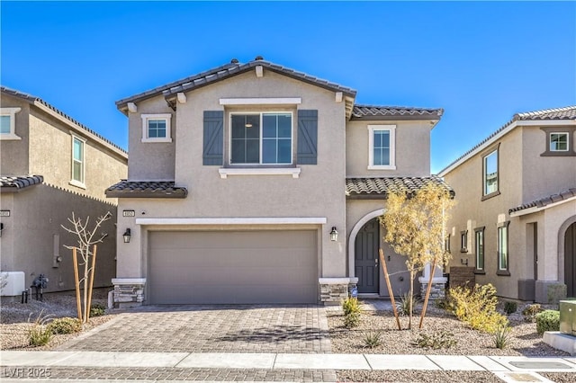 view of front of property featuring an attached garage, a tiled roof, stone siding, decorative driveway, and stucco siding