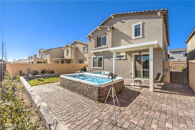 rear view of property with a fenced backyard, a patio, a hot tub, and stucco siding