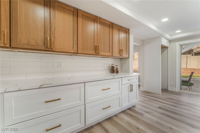 kitchen featuring white cabinetry, light hardwood / wood-style floors, light stone counters, and backsplash