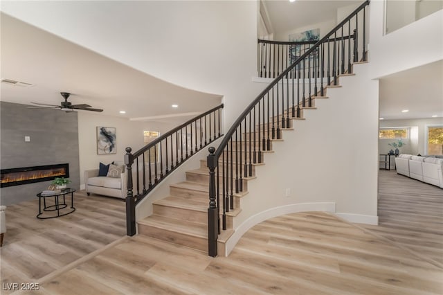 stairs featuring ceiling fan, a towering ceiling, wood-type flooring, and a fireplace