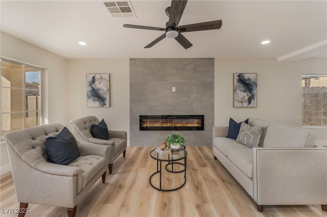 living room with ceiling fan, a fireplace, light hardwood / wood-style flooring, and a wealth of natural light