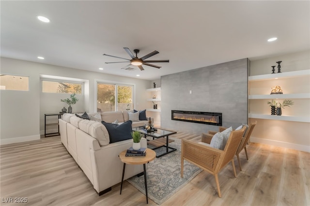 living room featuring ceiling fan, a fireplace, and light wood-type flooring