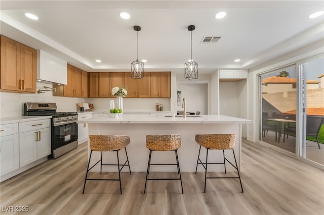 kitchen featuring decorative light fixtures, sink, white cabinets, a kitchen island with sink, and stainless steel gas range