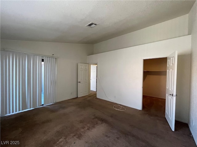 unfurnished bedroom featuring dark colored carpet, a walk in closet, a textured ceiling, and a closet