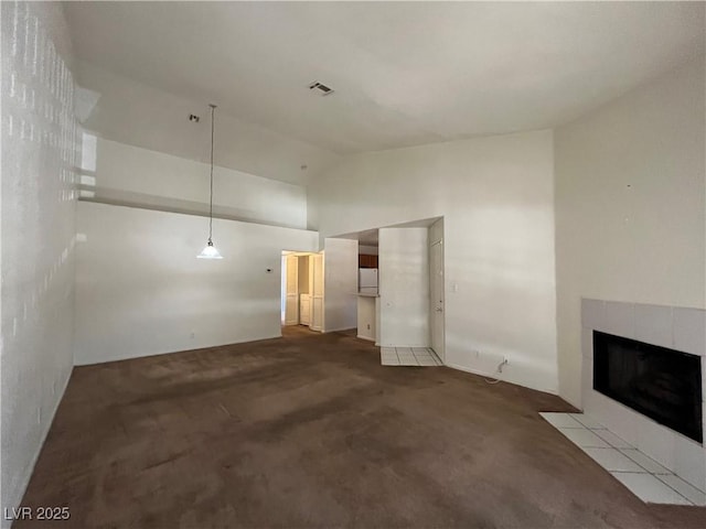 unfurnished living room with a tiled fireplace, dark colored carpet, and high vaulted ceiling