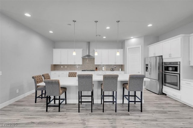 kitchen featuring decorative light fixtures, an island with sink, white cabinets, stainless steel appliances, and wall chimney exhaust hood