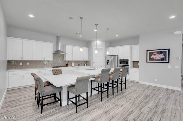 kitchen with wall chimney exhaust hood, a breakfast bar area, a large island with sink, appliances with stainless steel finishes, and white cabinets