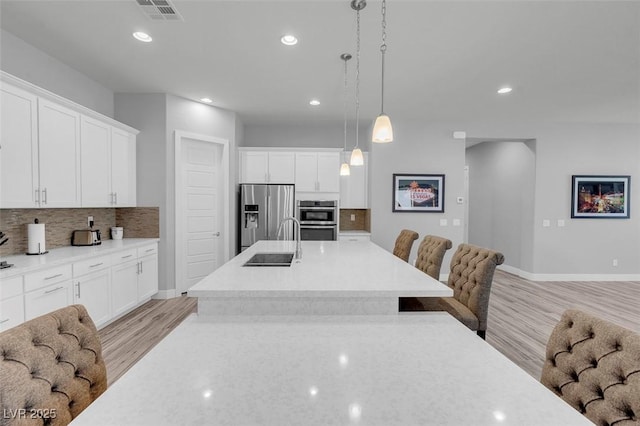 kitchen with tasteful backsplash, white cabinetry, sink, hanging light fixtures, and stainless steel appliances