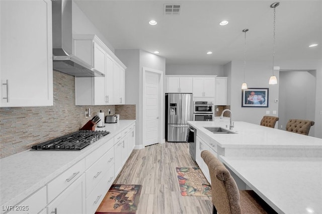 kitchen featuring sink, white cabinetry, decorative light fixtures, appliances with stainless steel finishes, and wall chimney range hood