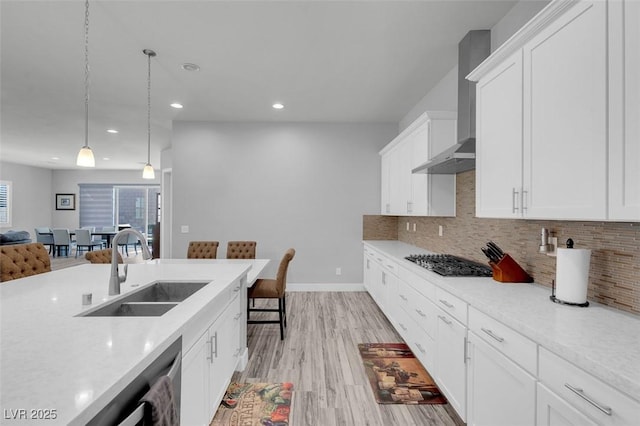 kitchen featuring appliances with stainless steel finishes, sink, white cabinets, hanging light fixtures, and wall chimney range hood