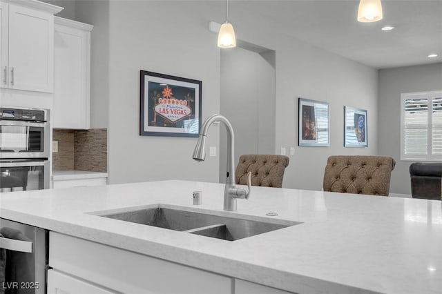 kitchen with sink, backsplash, hanging light fixtures, stainless steel appliances, and white cabinets