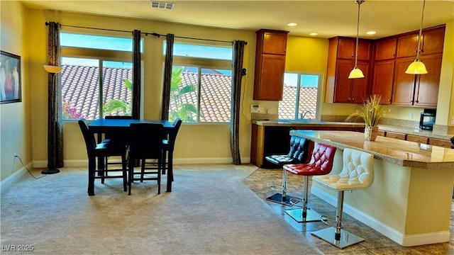 kitchen with decorative light fixtures, a breakfast bar area, and light colored carpet