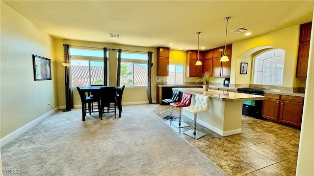 kitchen featuring a breakfast bar area, black range oven, hanging light fixtures, light colored carpet, and light stone countertops