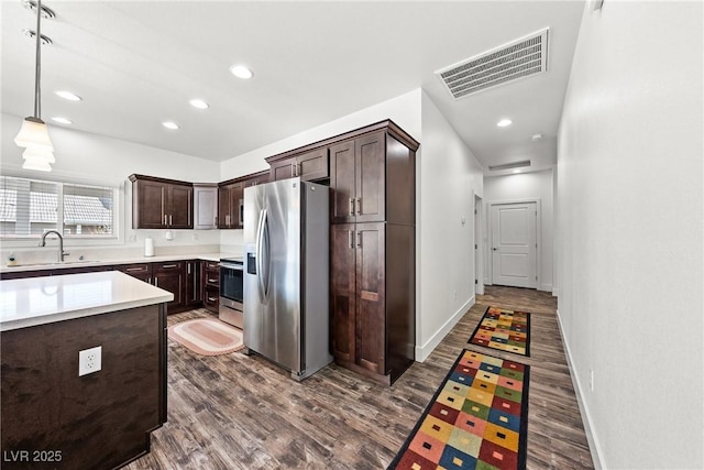 kitchen with sink, hanging light fixtures, dark brown cabinets, stainless steel appliances, and dark wood-type flooring