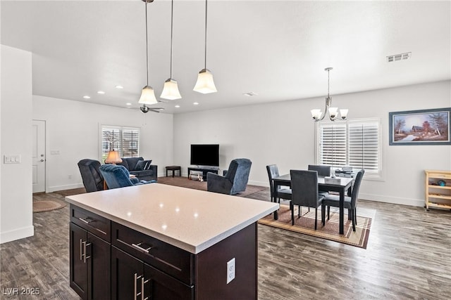 kitchen with a kitchen island, dark hardwood / wood-style floors, ceiling fan with notable chandelier, pendant lighting, and dark brown cabinetry