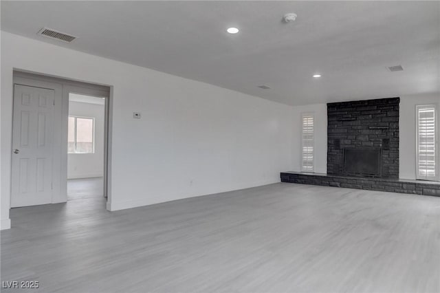 unfurnished living room featuring hardwood / wood-style floors, a brick fireplace, and a wealth of natural light