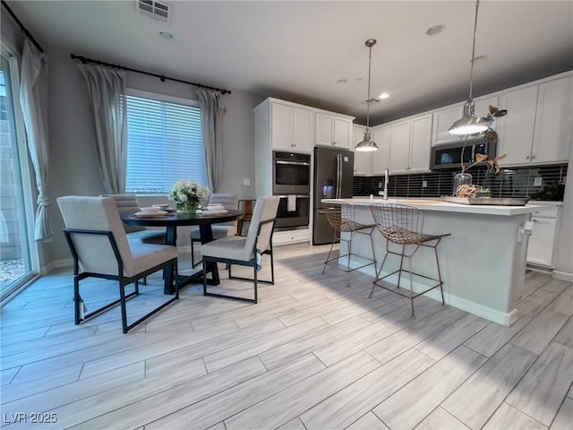 kitchen featuring appliances with stainless steel finishes, hanging light fixtures, white cabinets, and a center island with sink