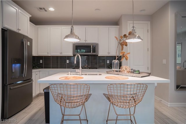 kitchen with white cabinetry, stainless steel appliances, hanging light fixtures, an island with sink, and a breakfast bar area