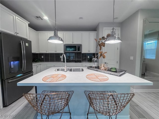 kitchen with a center island with sink, hanging light fixtures, white cabinetry, and black appliances