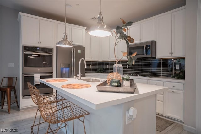 kitchen with a center island with sink, appliances with stainless steel finishes, white cabinets, and decorative light fixtures