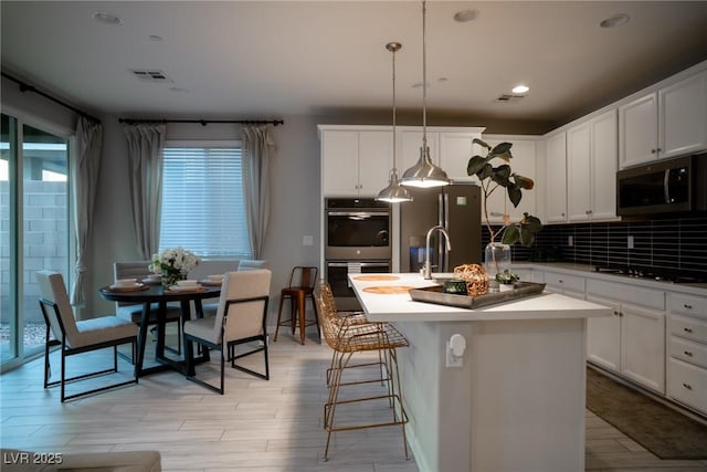 kitchen with a center island with sink, appliances with stainless steel finishes, white cabinetry, decorative light fixtures, and decorative backsplash