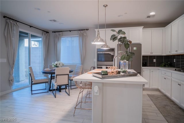 kitchen featuring stainless steel refrigerator, an island with sink, pendant lighting, and white cabinetry