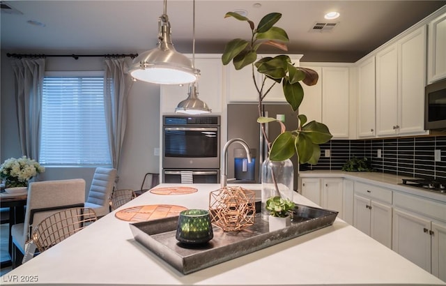 kitchen featuring appliances with stainless steel finishes, pendant lighting, white cabinetry, a kitchen breakfast bar, and tasteful backsplash