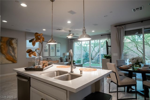 kitchen with white cabinetry, a center island with sink, decorative light fixtures, sink, and stainless steel dishwasher