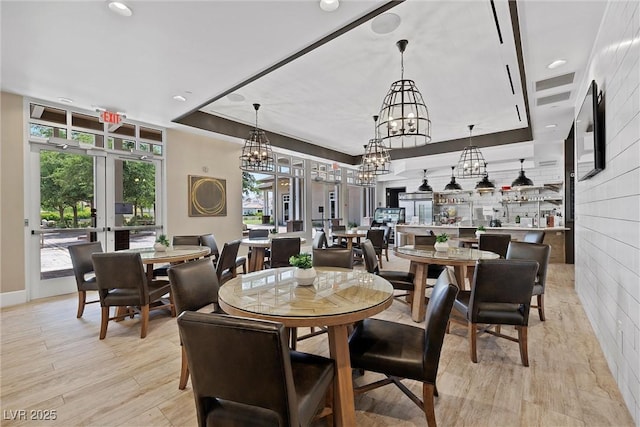 dining space with a raised ceiling, light hardwood / wood-style floors, and french doors