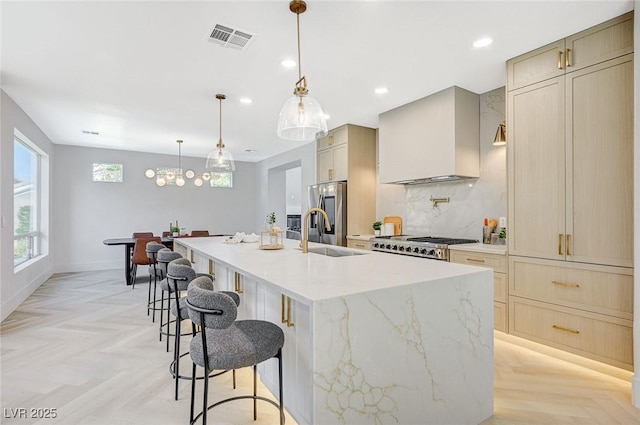 kitchen with sink, stainless steel fridge, an island with sink, wall chimney range hood, and light parquet floors