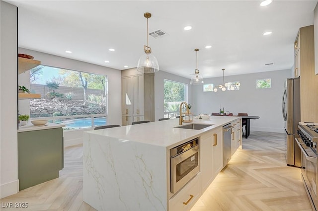 kitchen with sink, decorative light fixtures, appliances with stainless steel finishes, light parquet flooring, and a kitchen island with sink