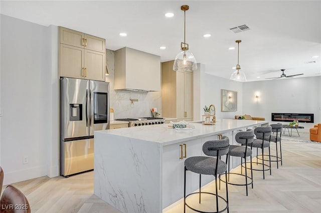 kitchen with wall chimney range hood, stainless steel fridge, a center island with sink, decorative light fixtures, and light parquet flooring